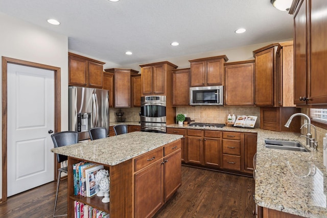 kitchen featuring sink, a breakfast bar area, a center island, appliances with stainless steel finishes, and light stone countertops