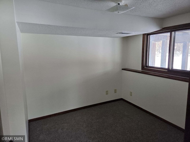 unfurnished room featuring dark carpet and a textured ceiling