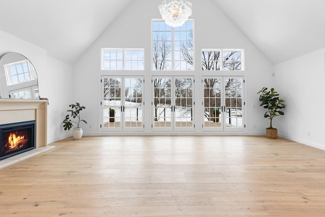 unfurnished living room with a towering ceiling, a notable chandelier, and light wood-type flooring