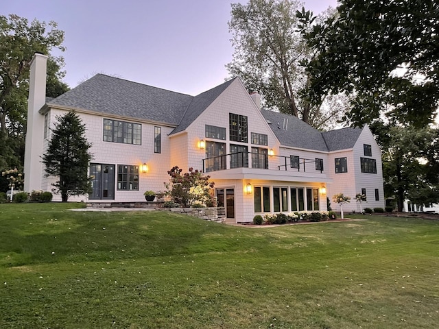 back house at dusk with a lawn and a balcony