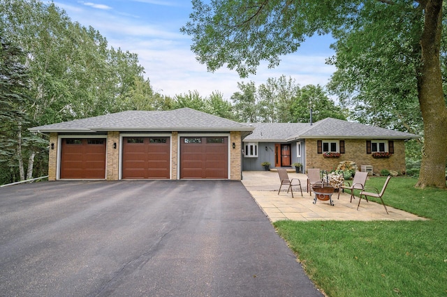 ranch-style house featuring brick siding, a fire pit, a front yard, a garage, and driveway