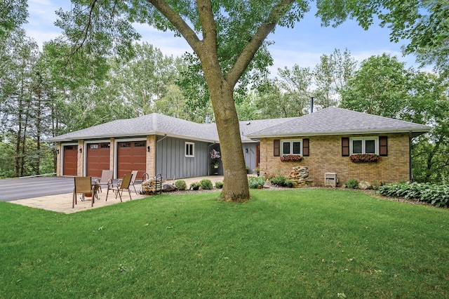 back of house with aphalt driveway, a yard, board and batten siding, an attached garage, and brick siding