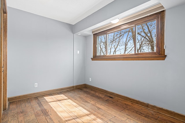 empty room with baseboards, visible vents, and hardwood / wood-style flooring