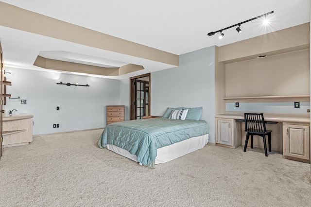 bedroom with a tray ceiling, light colored carpet, track lighting, and baseboards