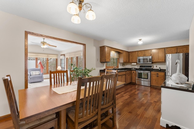 dining space with lofted ceiling, ceiling fan with notable chandelier, dark wood-type flooring, and a textured ceiling