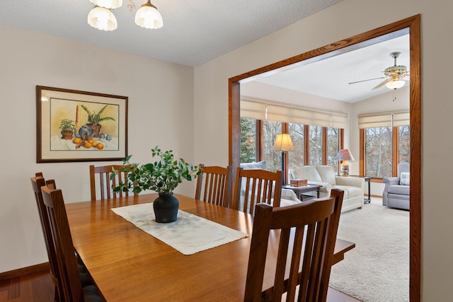 dining room featuring carpet floors, ceiling fan with notable chandelier, vaulted ceiling, and a textured ceiling