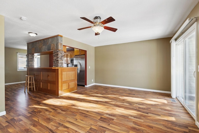 interior space with a breakfast bar area, wood finished floors, a ceiling fan, a peninsula, and stainless steel appliances