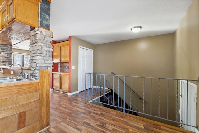 hallway with an upstairs landing, a sink, a textured ceiling, dark wood finished floors, and ornate columns