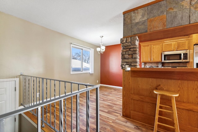 kitchen with stainless steel microwave, baseboards, a kitchen bar, light wood-style flooring, and an inviting chandelier