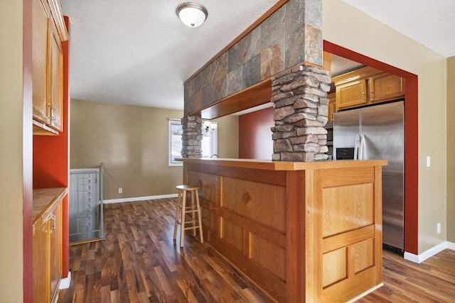 kitchen featuring baseboards, stainless steel fridge with ice dispenser, brown cabinets, a kitchen breakfast bar, and dark wood-style flooring