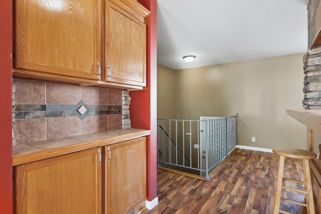 interior space with tasteful backsplash, baseboards, tile counters, brown cabinetry, and dark wood-style flooring