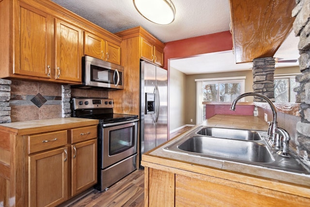 kitchen with wood finished floors, decorative columns, a sink, decorative backsplash, and stainless steel appliances