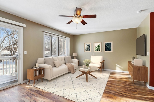 living area with light wood-style flooring, baseboards, a textured ceiling, and ceiling fan