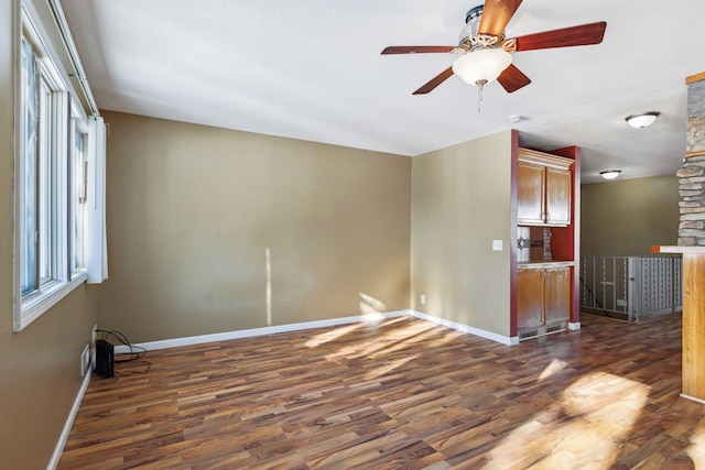 unfurnished room featuring dark wood finished floors, a ceiling fan, and baseboards