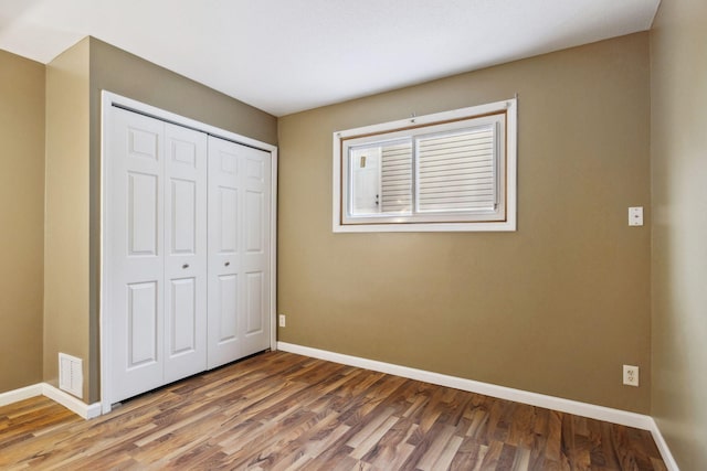 unfurnished bedroom featuring wood finished floors, baseboards, visible vents, and a closet