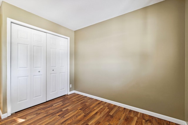 unfurnished bedroom featuring dark wood-type flooring, baseboards, and a closet