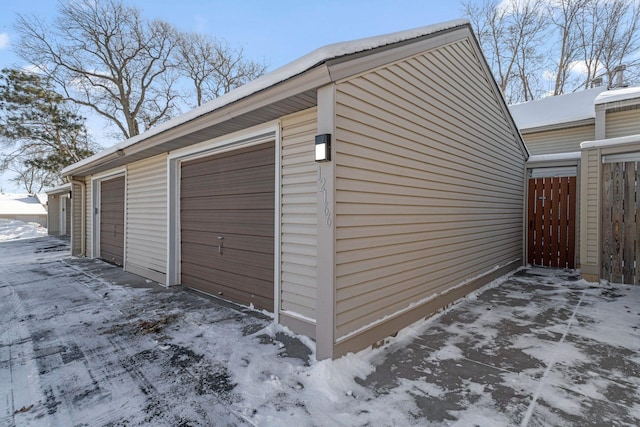 snow covered garage with a garage and fence