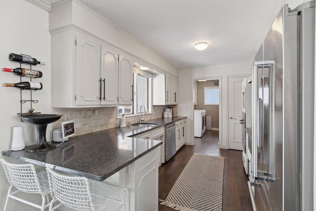 kitchen with sink, appliances with stainless steel finishes, white cabinetry, independent washer and dryer, and kitchen peninsula