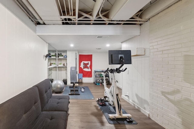 workout room with hardwood / wood-style flooring and brick wall