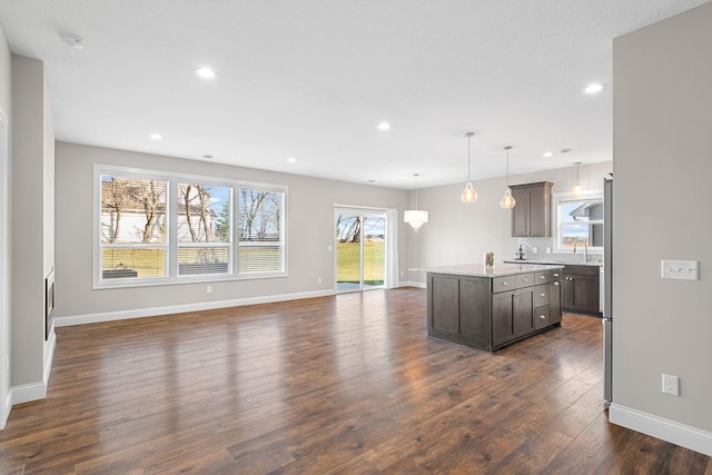 kitchen with decorative light fixtures, a center island, dark wood-type flooring, light stone countertops, and dark brown cabinets