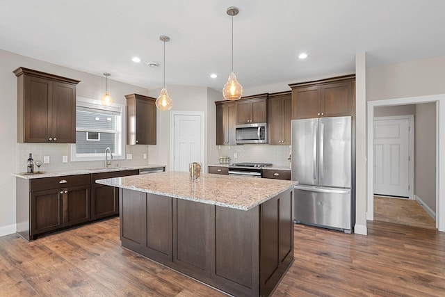 kitchen featuring sink, stainless steel appliances, light stone counters, a kitchen island, and decorative light fixtures