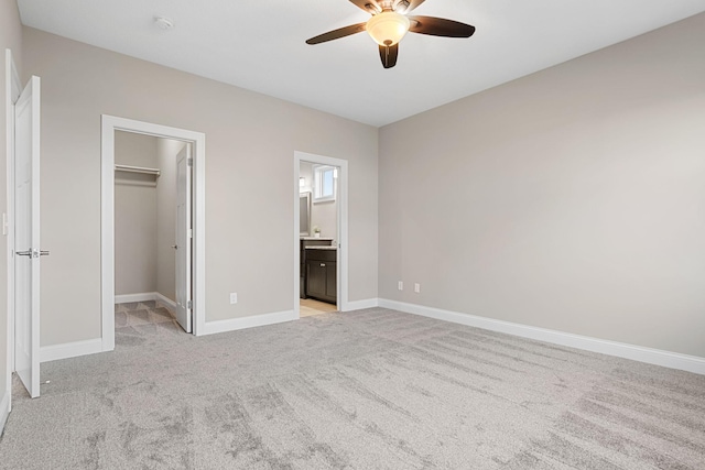 unfurnished bedroom featuring ensuite bathroom, a walk in closet, light carpet, a closet, and ceiling fan