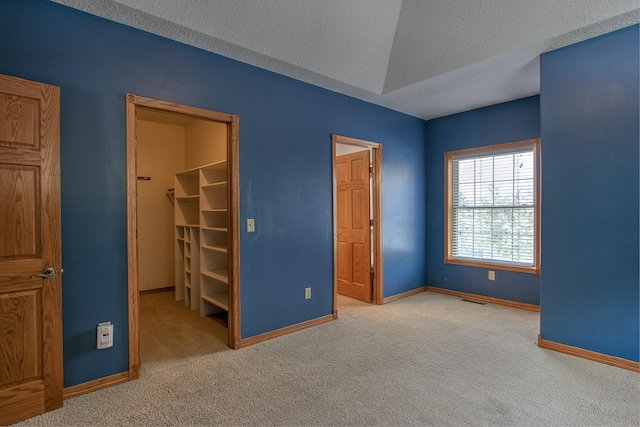 unfurnished bedroom with a spacious closet, a textured ceiling, and carpet