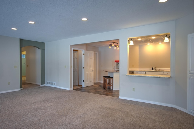 unfurnished living room featuring sink, a textured ceiling, and dark carpet