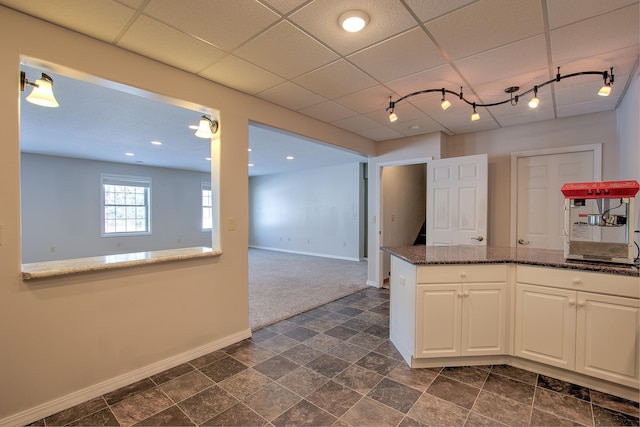 kitchen with white cabinets, dark stone counters, dark carpet, track lighting, and a drop ceiling