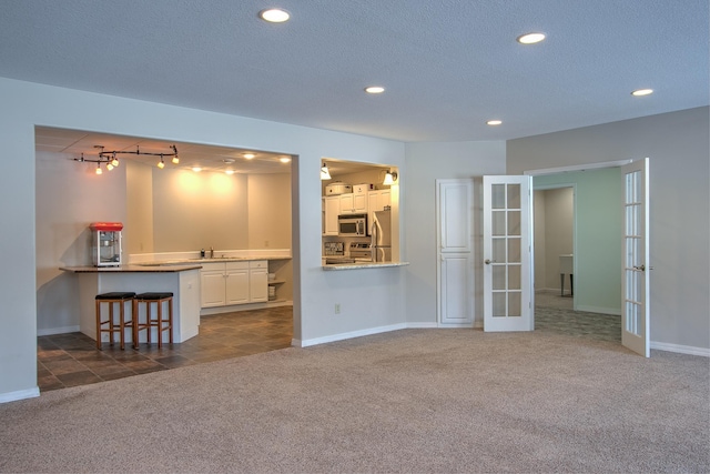 unfurnished living room with rail lighting, sink, dark colored carpet, a textured ceiling, and french doors