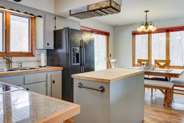 kitchen with pendant lighting, sink, butcher block counters, backsplash, and light wood-type flooring