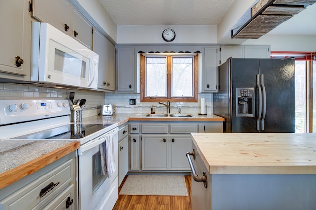 kitchen with wood counters, sink, white appliances, and a healthy amount of sunlight