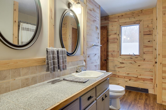 bathroom with wooden walls, vanity, wood-type flooring, decorative backsplash, and toilet