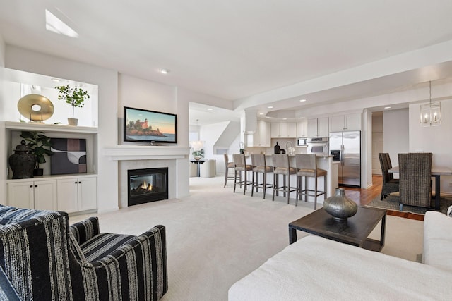 living area featuring carpet, an inviting chandelier, decorative columns, recessed lighting, and a glass covered fireplace