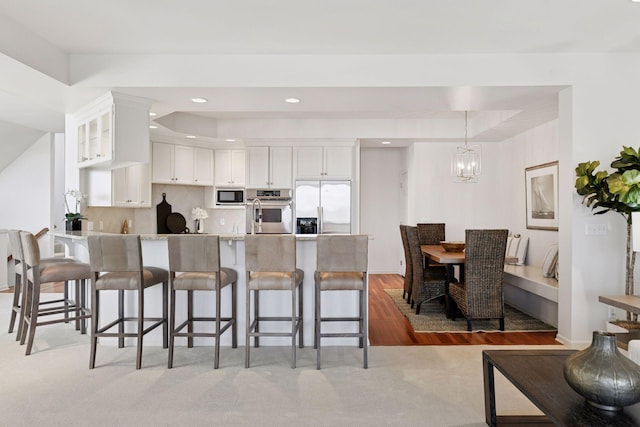 kitchen featuring a breakfast bar area, a peninsula, stainless steel appliances, white cabinets, and glass insert cabinets