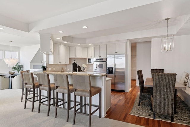 kitchen with wood finished floors, a peninsula, stainless steel appliances, a raised ceiling, and a notable chandelier