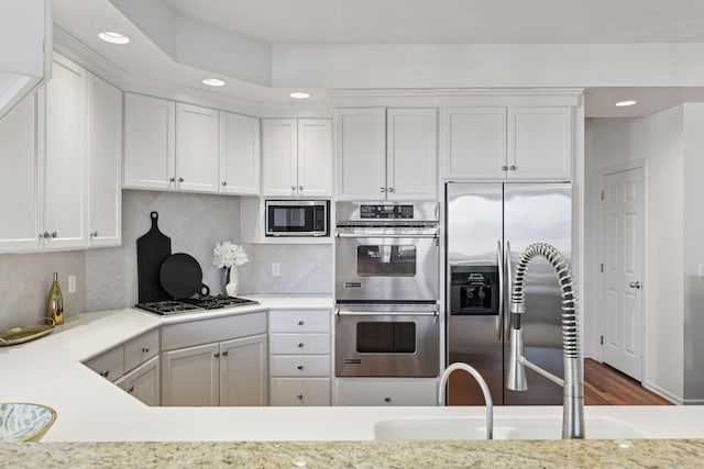 kitchen with tasteful backsplash, appliances with stainless steel finishes, white cabinetry, and light countertops