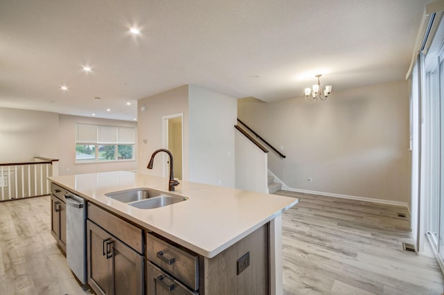 kitchen featuring an island with sink, dishwasher, sink, and light wood-type flooring