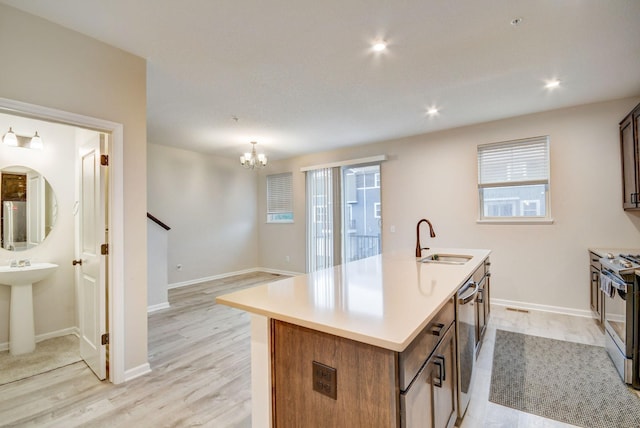 kitchen with sink, a center island with sink, stainless steel range, and light hardwood / wood-style floors