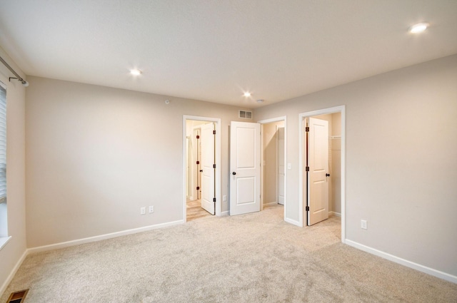 unfurnished bedroom with connected bathroom, a spacious closet, and light carpet