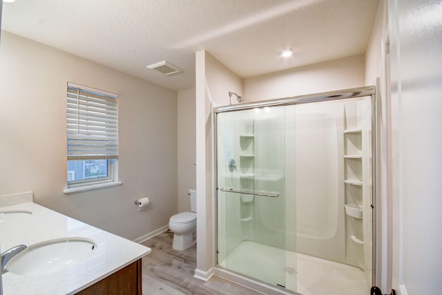 bathroom featuring vanity, wood-type flooring, a textured ceiling, a shower with shower door, and toilet