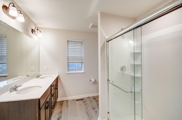 bathroom with hardwood / wood-style floors, vanity, walk in shower, a healthy amount of sunlight, and a textured ceiling