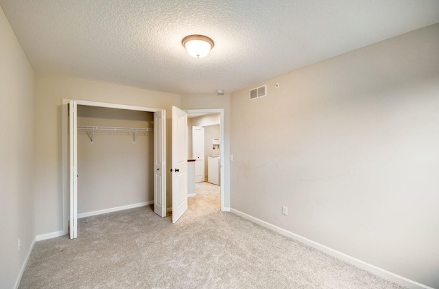 unfurnished bedroom with washer / clothes dryer, light colored carpet, a closet, and a textured ceiling