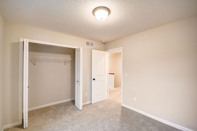 unfurnished bedroom with light carpet, a textured ceiling, and a closet