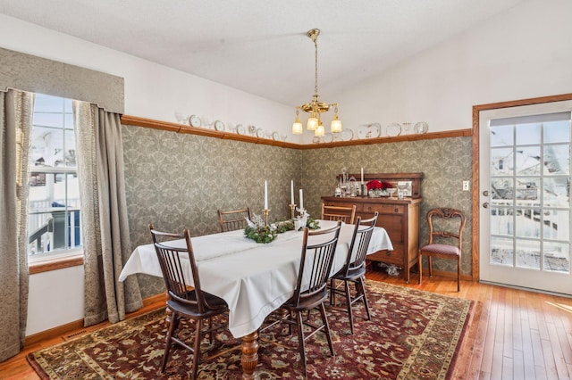 dining area with an inviting chandelier, vaulted ceiling, and wood-type flooring