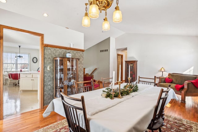 dining area with light wood-type flooring, lofted ceiling, and an inviting chandelier