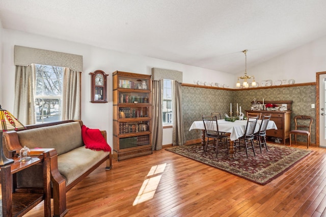 dining space with a notable chandelier, vaulted ceiling, a textured ceiling, and hardwood / wood-style floors