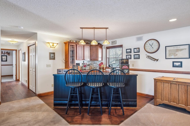 kitchen featuring kitchen peninsula, decorative light fixtures, a breakfast bar area, a textured ceiling, and dark hardwood / wood-style floors