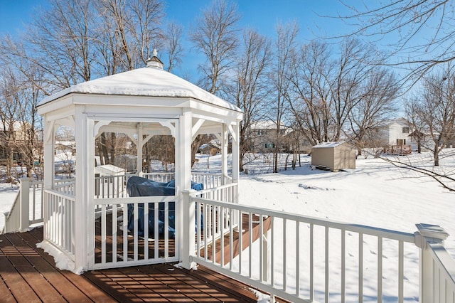 snow covered deck featuring a storage shed and a gazebo