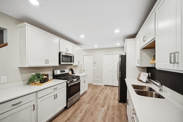 kitchen featuring white cabinetry, stainless steel appliances, sink, and light hardwood / wood-style flooring